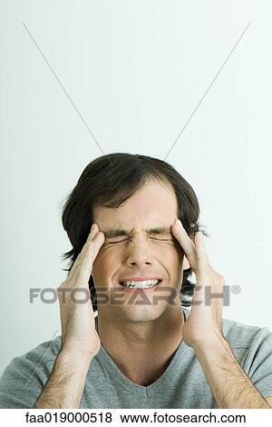 Stock Photo - Man, holding sides of head and squinting eyes shut, portrait. Fotosearch
