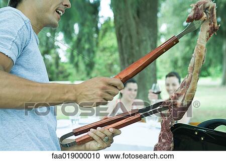 Man holding up piece of meat over barbecue View Large Photo Image Stock Image - Man holding up piece of meat over barbecue. Fotosearch