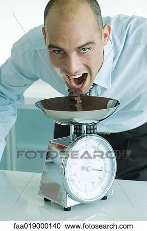 Man leaning toward stack of chocolate chunks on kitchen scale with mouth wide open View Large Photo Image Stock Image - Man leaning toward stack of chocolate chunks on kitchen scale with mouth wide open. Fotosearch