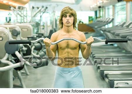Man lifting barbell in weight room, front view View Large Photo Image Stock Image - Man lifting barbell in weight room, front view. Fotosearch