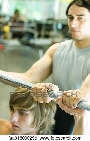 Stock Photography - Man lifting barbell while second man spots. Fotosearch