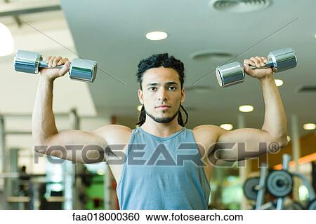 Stock Image - Man lifting dumbbells, waist up, front view. Fotosearch