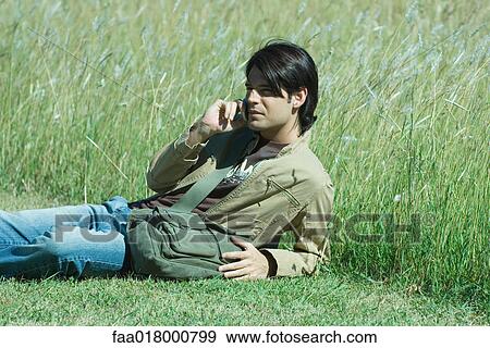 Man lying in grass, using cell phone View Large Photo Image Stock Photo - Man lying in grass, using cell phone. Fotosearch