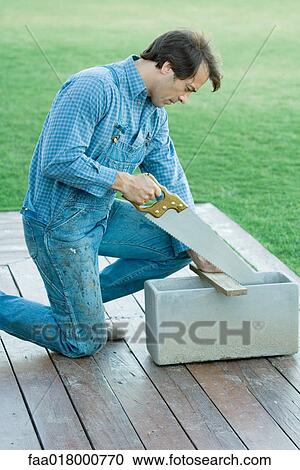 Stock Image - Man sawing piece of wood. Fotosearch