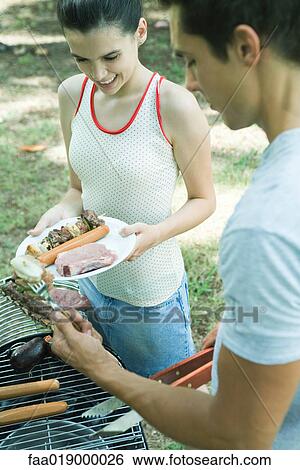 Stock Photograph - Man serving teen girl grilled meats from barbecue. Fotosearch