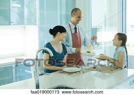 Stock Image - Man serving wife and daughter spaghetti. Fotosearch