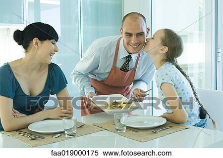 Stock Photography - Man serving wife and daughter spaghetti, girl kissing father on cheek. Fotosearch