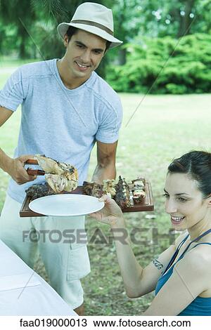 Man serving woman grilled meat during cookout View Large Photo Image Stock Image - Man serving woman grilled meat during cookout. Fotosearch