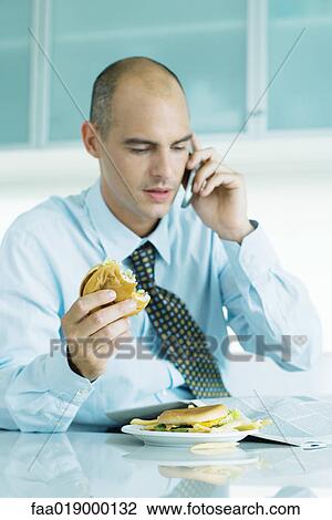 Man sitting at table eating hamburgers, reading newspaper and using cell phone View Large Photo Image Stock Image - Man sitting at table eating hamburgers, reading newspaper and using cell phone . Fotosearch