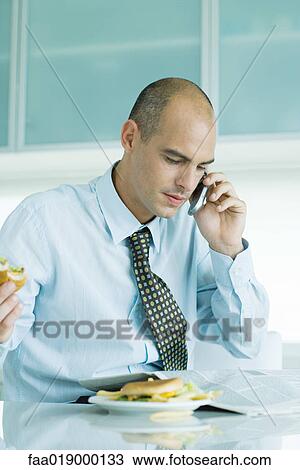 Man sitting at table eating hamburgers, reading newspaper and using cell phone View Large Photo Image Stock Image - Man sitting at table eating hamburgers, reading newspaper and using cell phone . Fotosearch
