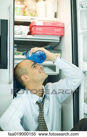 Man sitting in front of open refrigerator, holding bottle of water on forehead View Large Photo Image Stock Photography - Man sitting in front of open refrigerator, holding bottle of water on forehead. Fotosearch