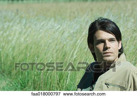 Stock Photo - Man sitting in long grass, looking away. Fotosearch