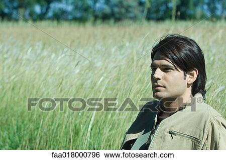 Stock Photograph - Man sitting in long grass, looking away. Fotosearch