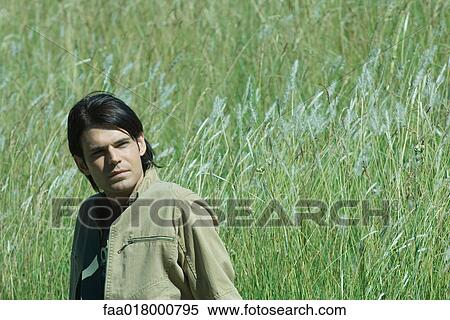 Stock Photography - Man sitting in long grass, looking away. Fotosearch