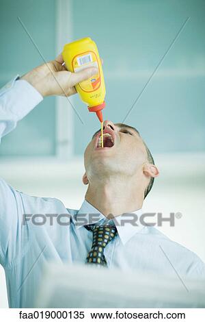 Stock Photography - Man squeezing mustard into mouth. Fotosearch