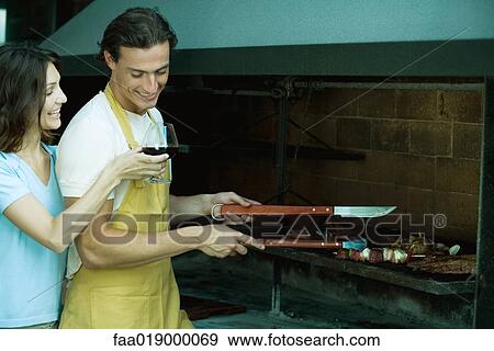 Man tending barbecue, while woman holds up glass of wine for him View Large Photo Image Stock Photo - Man tending barbecue, while woman holds up glass of wine for him. Fotosearch