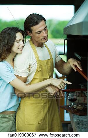 Man tending barbecue, while woman looks over his shoulder and points View Large Photo Image Stock Photo - Man tending barbecue, while woman looks over his shoulder and points. Fotosearch