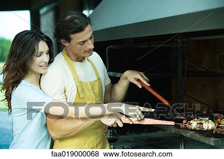 Man tending barbecue, while woman looks over his shoulder and points View Large Photo Image Stock Photo - Man tending barbecue, while woman looks over his shoulder and points. Fotosearch