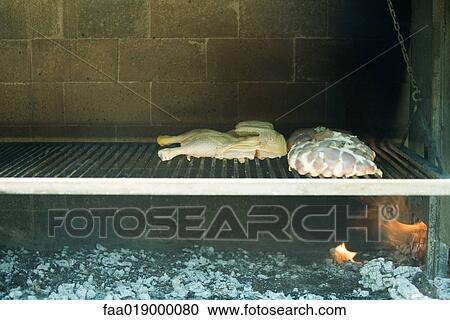 Stock Image - Meats grilling in wood oven. Fotosearch