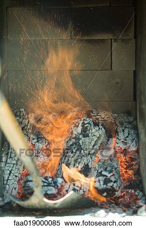 Stock Photography - Person shoveling logs in wood oven . Fotosearch