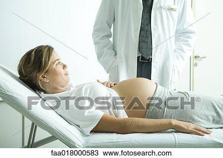 Stock Image - Pregnant woman lying on back, doctor standing next to her. Fotosearch