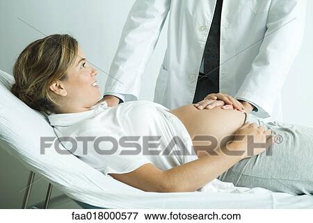 Stock Photo - Pregnant woman lying on back, doctor's hand on stomach. Fotosearch