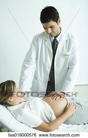 Stock Photograph - Pregnant woman lying on back, doctor's hand on stomach. Fotosearch
