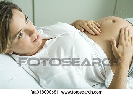 Stock Image - Pregnant woman lying on back, hands on stomach. Fotosearch