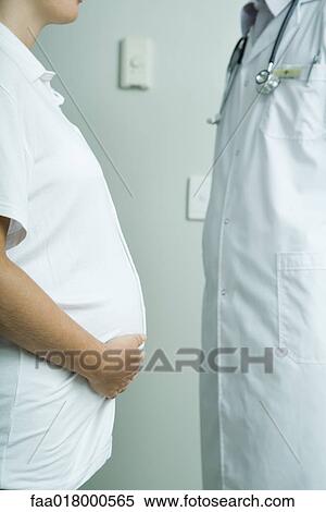 Pregnant woman standing face to face with doctor, mid section, side view View Large Photo Image Stock Photography - Pregnant woman standing face to face with doctor, mid section, side view. Fotosearch