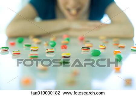 Table spread with candy, woman resting head on arms, holding piece of candy between teeth View Large Photo Image Stock Image - Table spread with candy, woman resting head on arms, holding piece of candy between teeth. Fotosearch