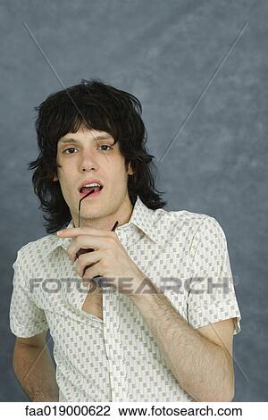 Stock Image - Teen boy holding sunglasses to lip, looking at camera, portrait. Fotosearch