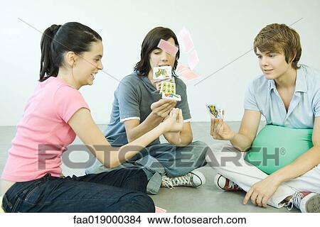 Picture - Teen friends playing cards, one throwing cards into the air. Fotosearch
