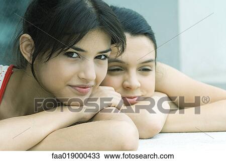 Stock Image - Teen girl and young woman resting heads on arms, smiling. Fotosearch