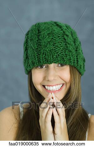 Stock Photography - Teen girl wearing knit hat, hands clasped in front of chin, smiling at camera, portrait. Fotosearch