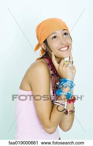 Teen girl wearing lots of accessories, fingers at sides of cheeks, looking up View Large Photo Image Stock Image - Teen girl wearing lots of accessories, fingers at sides of cheeks, looking up. Fotosearch
