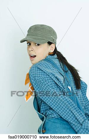 Teen girl wearing overalls and cap, looking over shoulder at camera View Large Photo Image Stock Image - Teen girl wearing overalls and cap, looking over shoulder at camera. Fotosearch