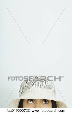 Stock Image - Teen girl wearing sun hat, looking up, cropped view, portrait. Fotosearch