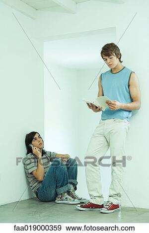 Teenage boy using cell phone while friend looks at book View Large Photo Image Stock Photo - Teenage boy using cell phone while friend looks at book. Fotosearch