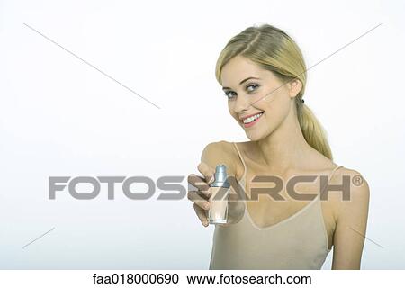 Stock Image - Teenage girl applying foundation, holding bottle out toward camera. Fotosearch