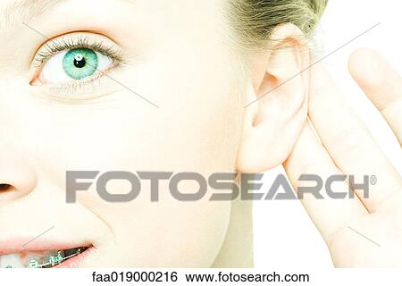 Stock Photograph - Teenage girl holding hand behind ear, looking at camera, smiling, close-up. Fotosearch