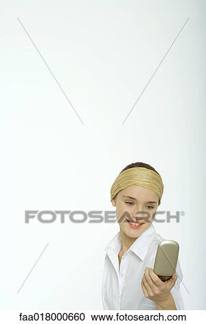Stock Image - Teenage girl looking at face in hand mirror. Fotosearch
