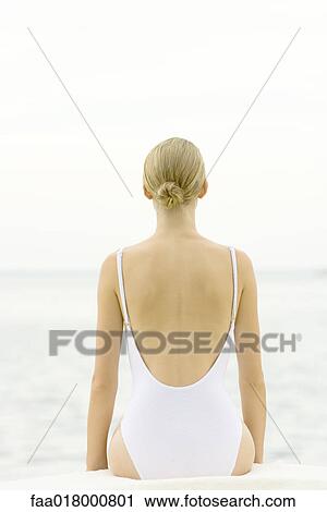 Stock Image - Teenage girl sitting on beach, rear view. Fotosearch