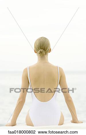Stock Image - Teenage girl sitting, wearing bathing suit, rear view. Fotosearch