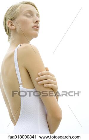 Stock Image - Teenage girl wearing bathing suit, hand on shoulder, eyes closed. Fotosearch