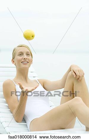 Picture - Teenage girl wearing bathing suit, tossing apple into air. Fotosearch