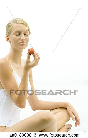 Stock Image - Teenage girl wearing bathing suit, holding up strawberry. Fotosearch