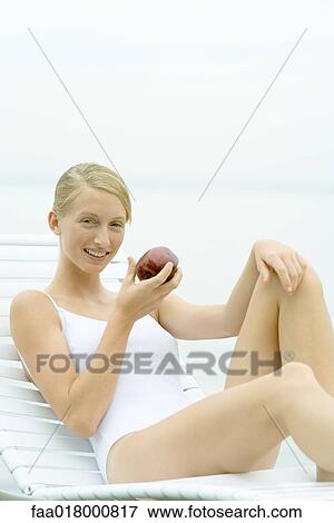 Teenage girl wearing bathing suit, sitting in lounge chair, holding apple View Large Photo Image Stock Photo - Teenage girl wearing bathing suit, sitting in lounge chair, holding apple. Fotosearch