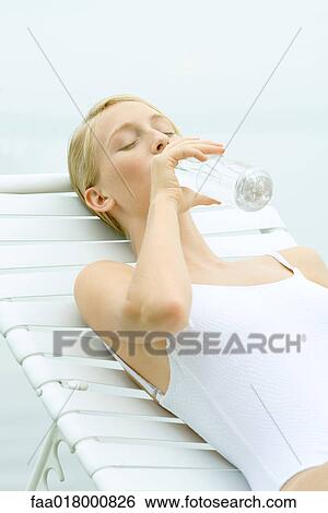 Stock Photograph - Teenage girl wearing bathing suit, sitting in lounge chair, drinking from bottle of water, eyes closed. Fotosearch