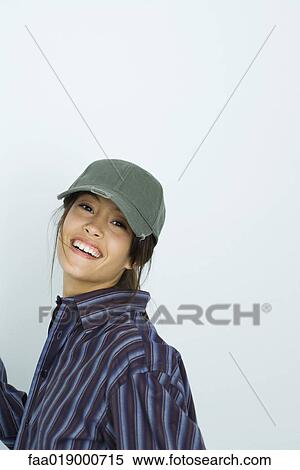 Stock Photography - Teenage girl wearing large button down shirt and baseball cap, portrait. Fotosearch
