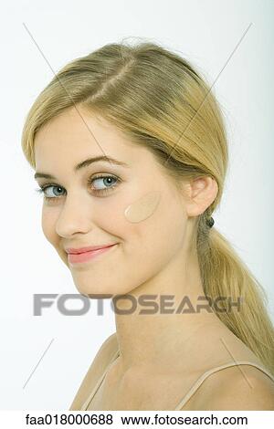 Stock Photo - Teenage girl with dollop of foundation on cheek, smiling at camera. Fotosearch